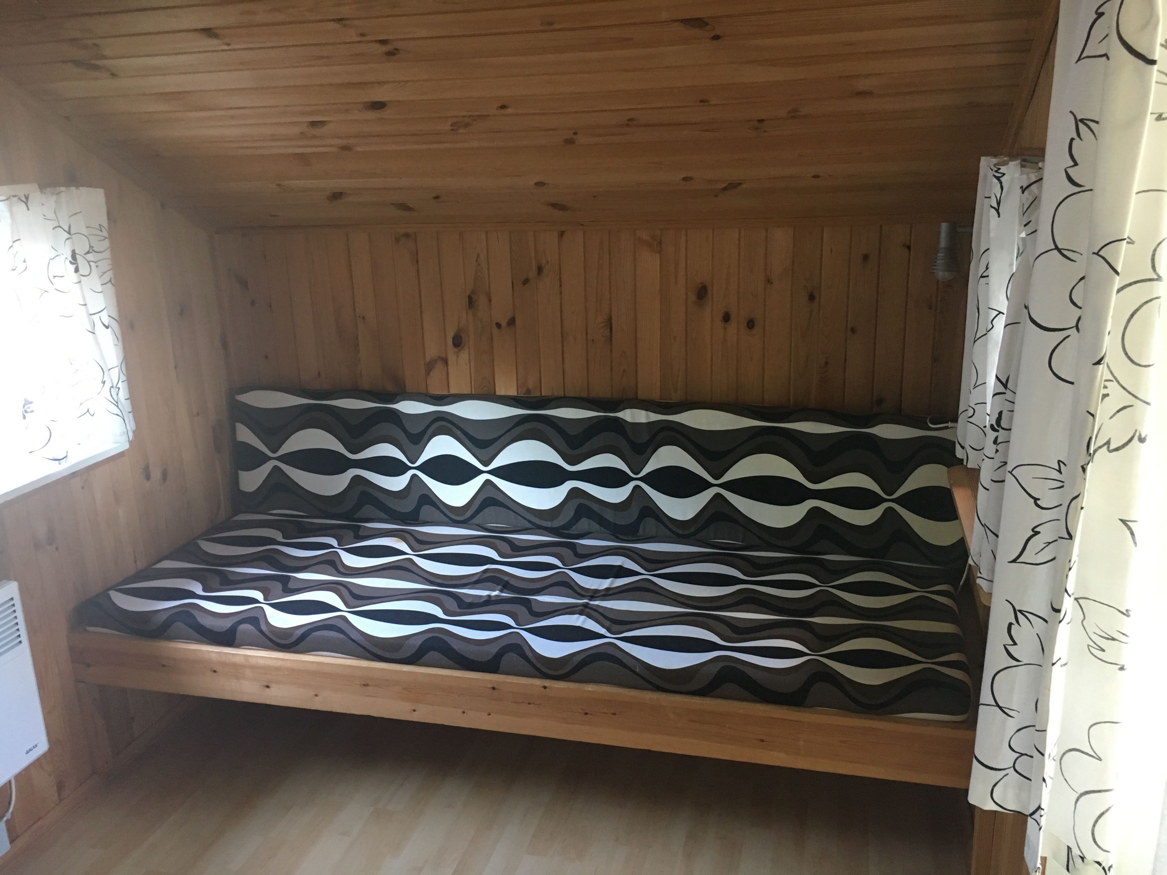 A wooden cabin with a bed featuring a black and white wavy pattern.