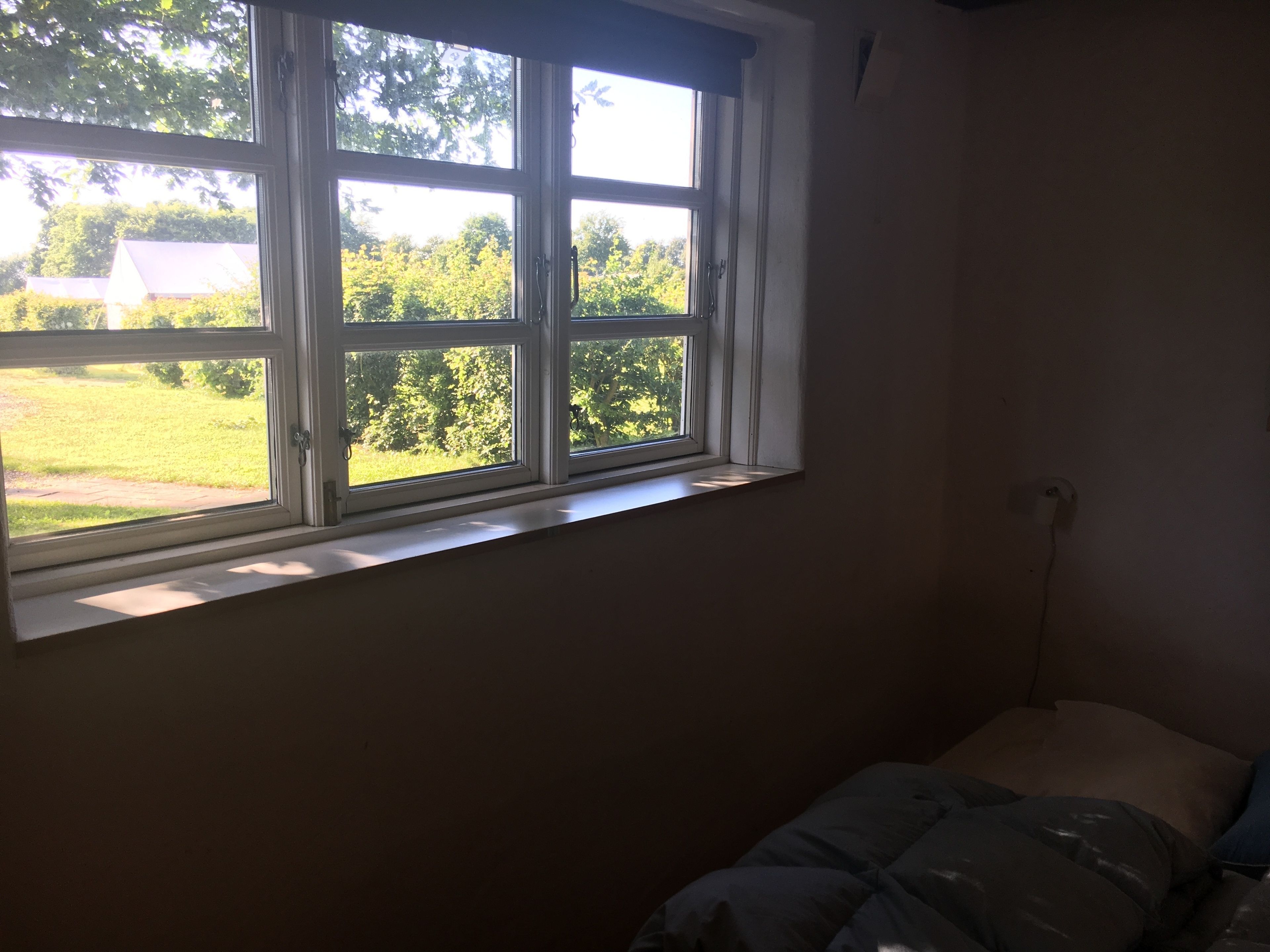 A room with a large window, a bed, and a wall socket.