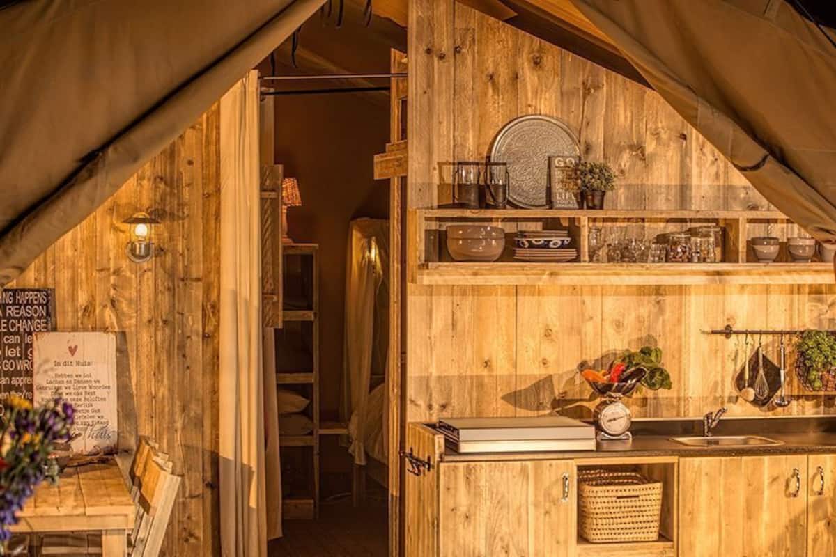 A rustic kitchen with wooden walls and shelves, a sink, and various kitchenware.