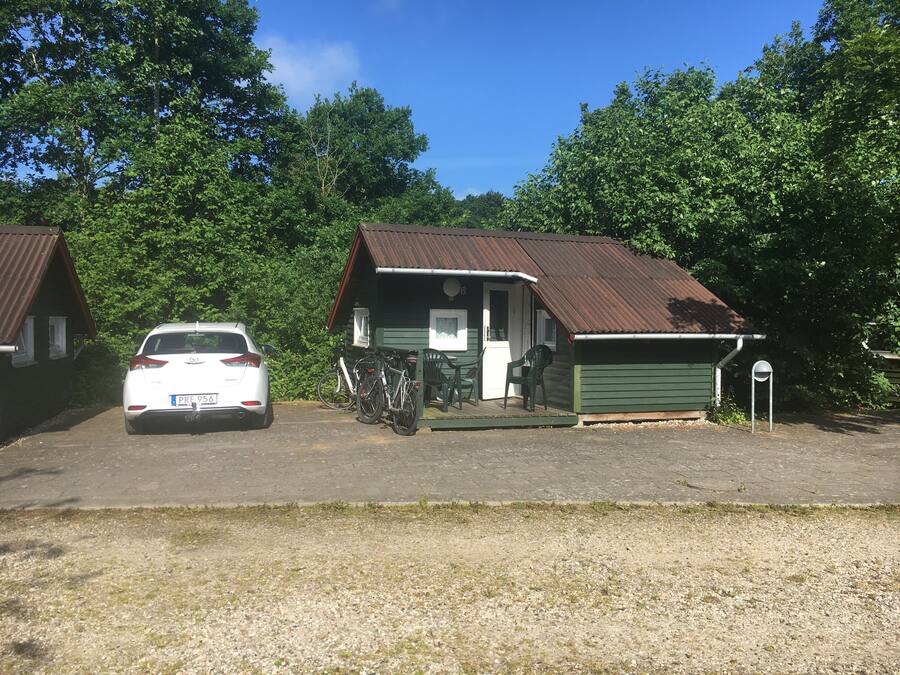 A two-story building with a green exterior and a brown roof, featuring a small porch with chairs and a table.