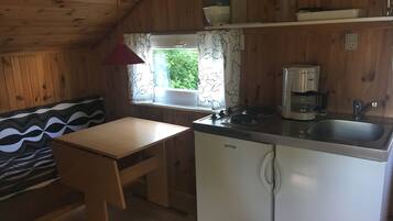 A compact kitchen with wooden walls, a window with curtains, a sink, a coffee maker, and a refrigerator.