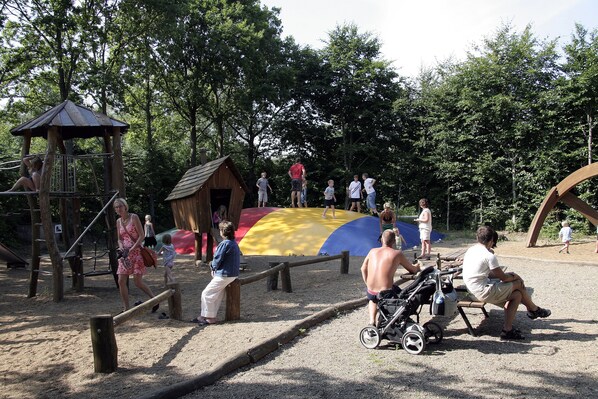 Un parque infantil con un módulo de juegos de madera, un tobogán grande y un pequeño refugio.