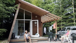 A wooden cabin with a large glass door, outdoor seating, and a car parked nearby. - Dancamps Trelde Næs (Fredericia)
