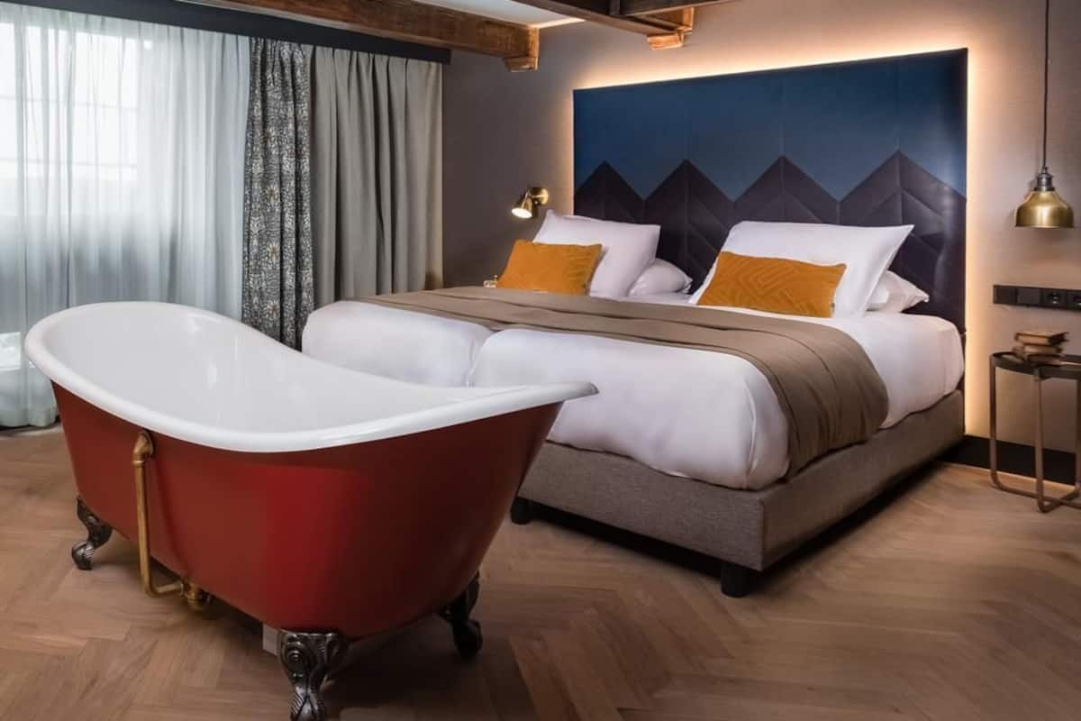 Quarto de hotel moderno com uma cama grande, uma banheira de imersão vermelha e um mural de parede extenso.