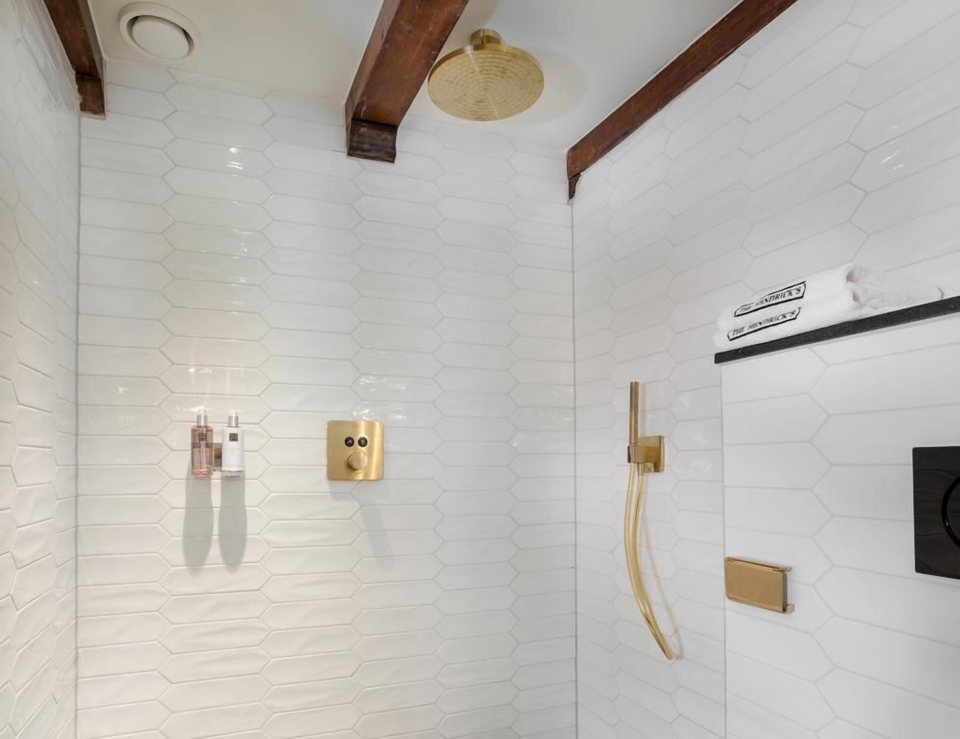Un baño moderno con baldosas blancas hexagonales, un cabezal de ducha dorado y un perchero para toallas.