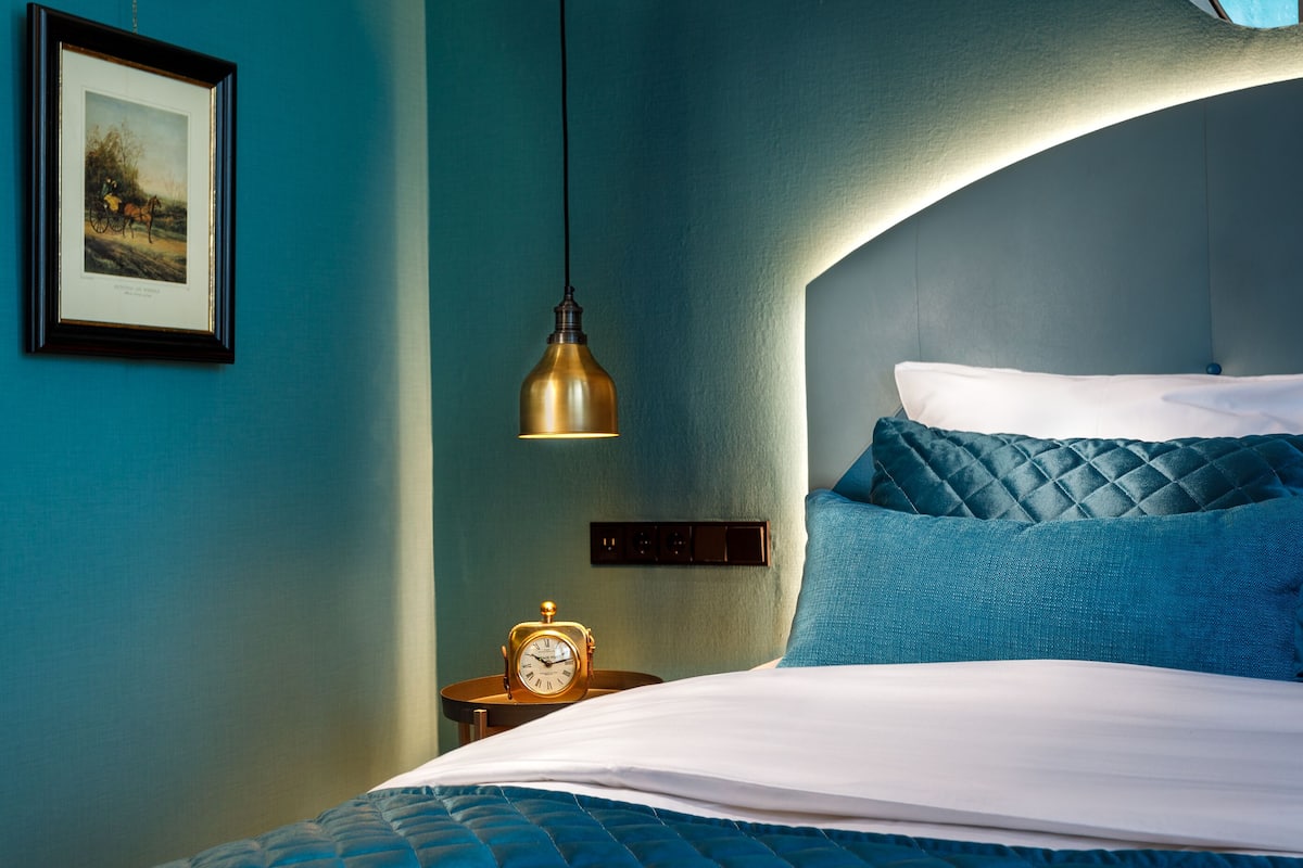 Quarto com cama, relógio, quadro emoldurado e luminária pendente.