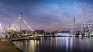 A waterfront marina with several boats docked, a large illuminated building, and a clear sky. - The Hendrick's Hotel (Amsterdam)