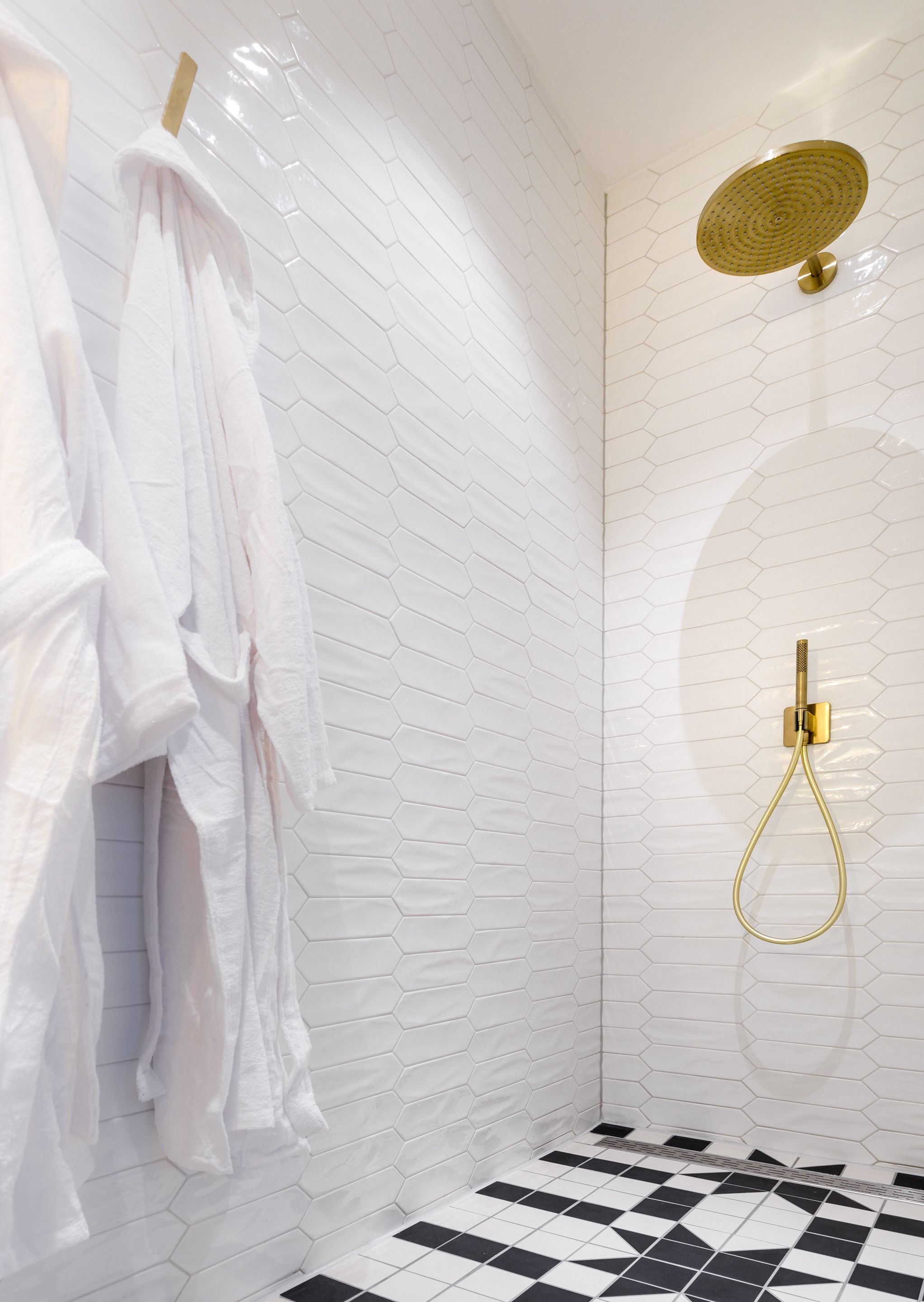 Un bagno moderno con piastrelle bianche esagonali, un soffione dorato e un pavimento a scacchi bianconero.