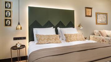 A hotel room with a large bed, a nightstand with a clock, a wall-mounted lamp, and framed artwork.