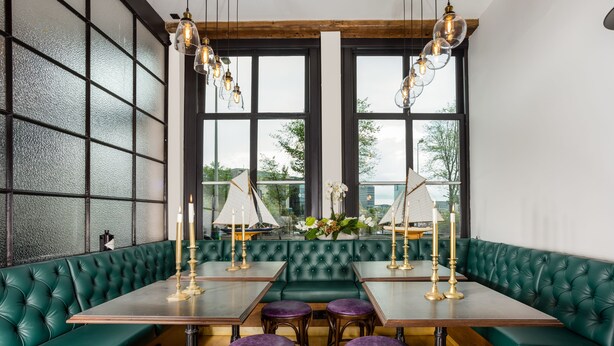 A restaurant with green upholstered booths, wooden tables, and purple stools. - The Hendrick's Hotel (Amsterdam)