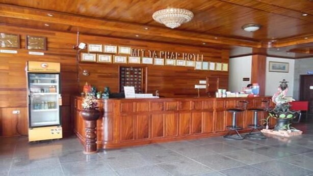 A reception area with a wooden reception desk, a refrigerator, and a chandelier. - Friendship Hotel (Oudomxay)