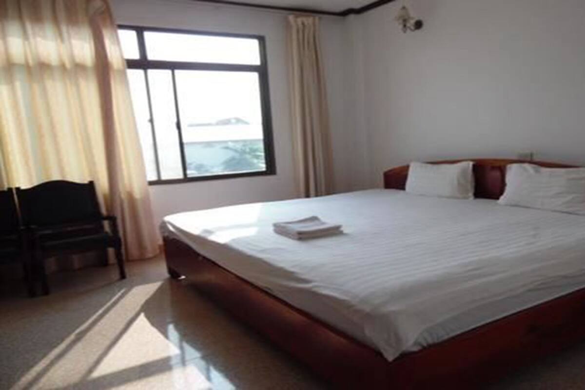 Une chambre d’hôtel avec un grand lit, une chaise et une fenêtre avec des rideaux.
