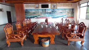 A conference room with a large wooden table surrounded by ornate chairs, a television mounted on the wall, and a large painting depicting a landscape. - Friendship Hotel (Oudomxay)