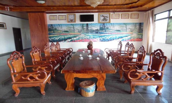 A conference room with a large wooden table surrounded by ornate chairs, a television mounted on the wall, and a large painting depicting a landscape. - Friendship Hotel (Oudomxay)