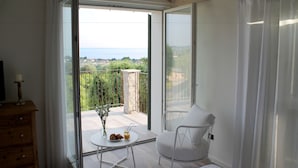 A bedroom with a balcony, a wooden dresser, a white chair, and a table with a vase of flowers and croissants. - Ca' Muretta Relais (Bardolino)