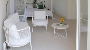 A bedroom with a four-poster bed, two white chairs, a small round table with a book and flowers, and a floor lamp. - Ca' Muretta Relais (Bardolino)