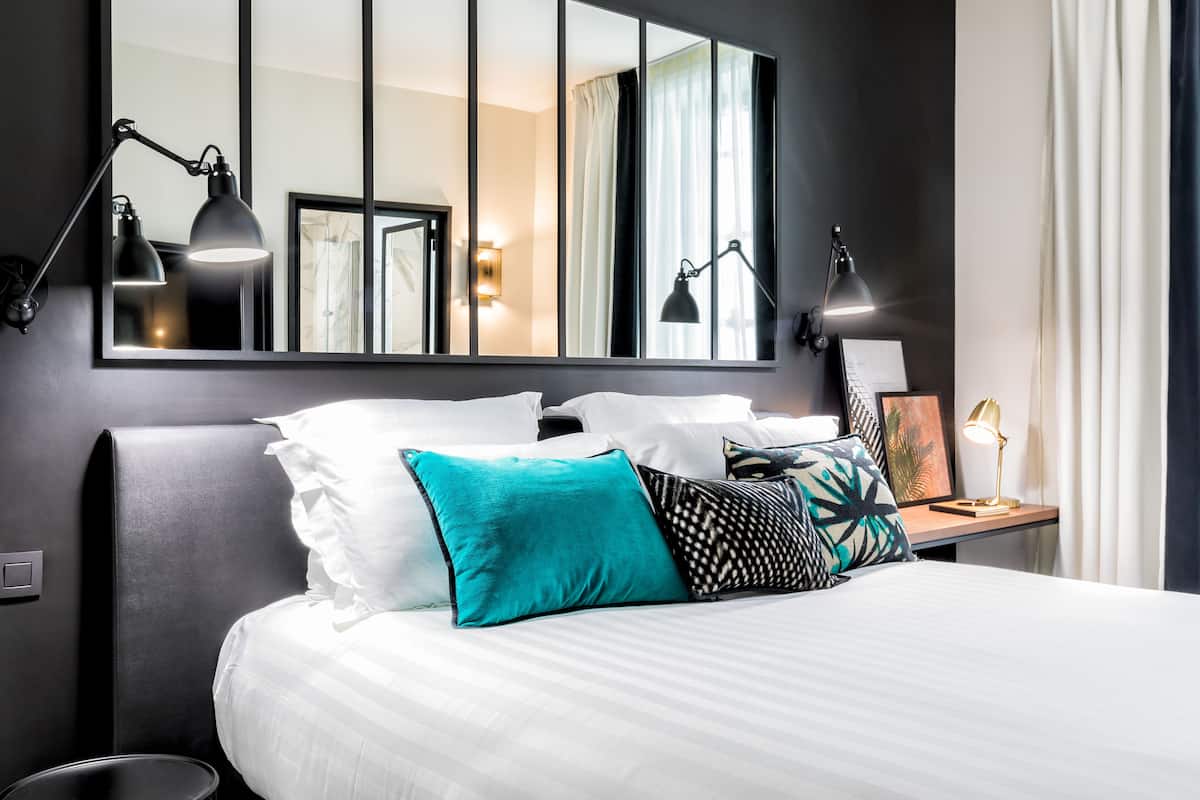Una habitación de hotel moderna con una cama grande, dos lámparas de noche, una mesita de noche con lámpara y un espejo grande en la pared.