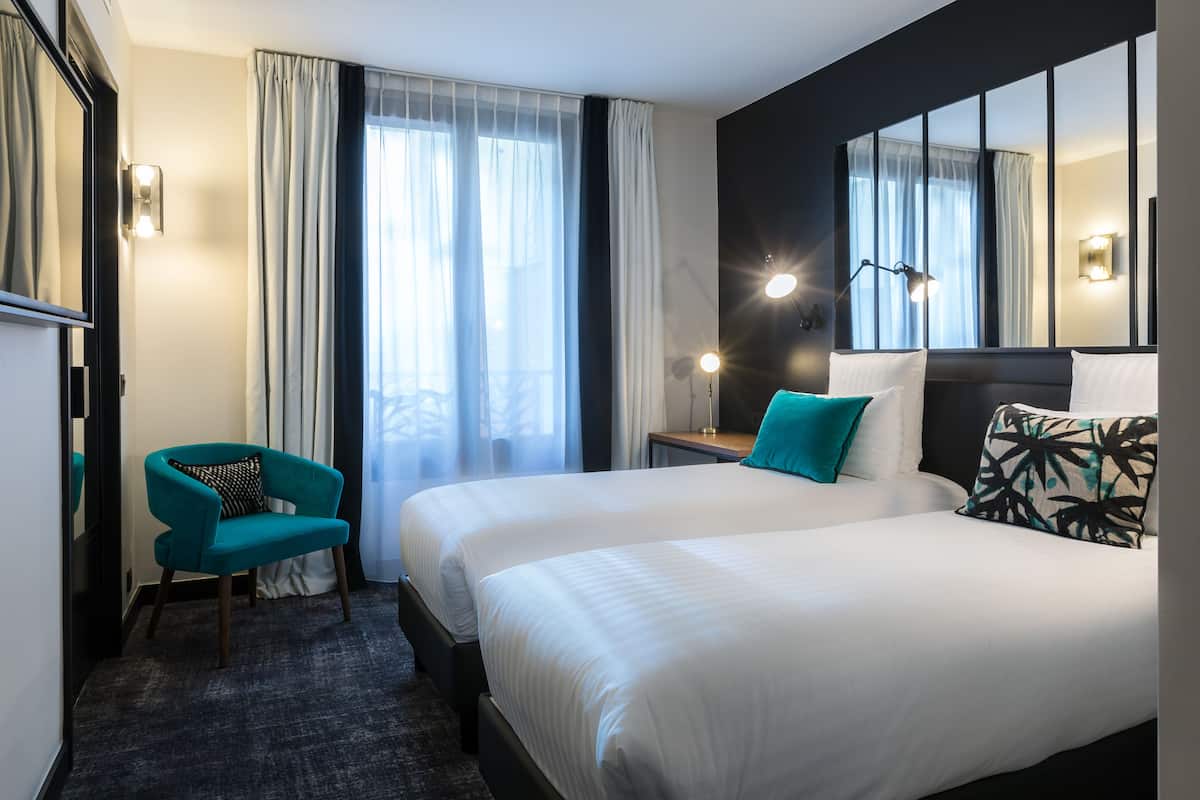 Una habitación de hotel con dos camas, una silla, una mesita de noche y un espejo grande.