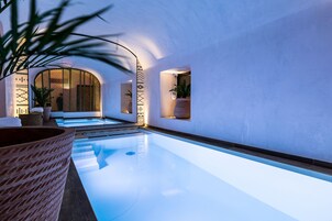 Una piscina interior moderna con superficie de agua cristalina, rodeada de paredes blancas y decoración minimalista.