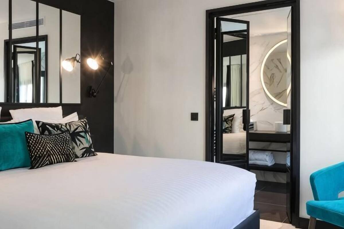 Una habitación de hotel moderna con una cama grande, un armario, un espejo y una silla azul.
