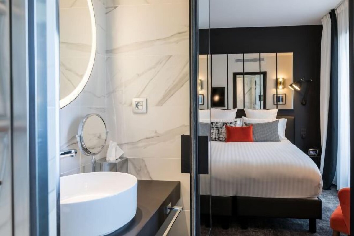 A modern hotel room with a marble bathroom, a large bed with pillows, and a bedside table.