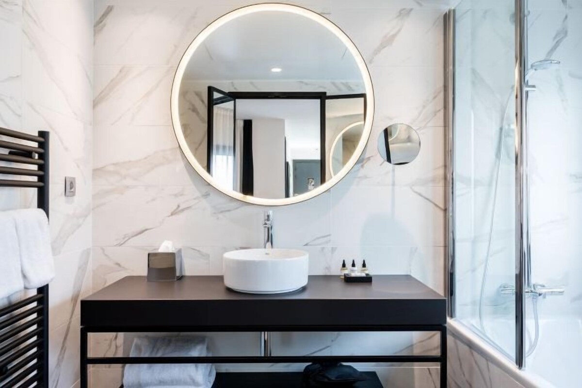A bathroom with a round mirror, a sink, and a shower.