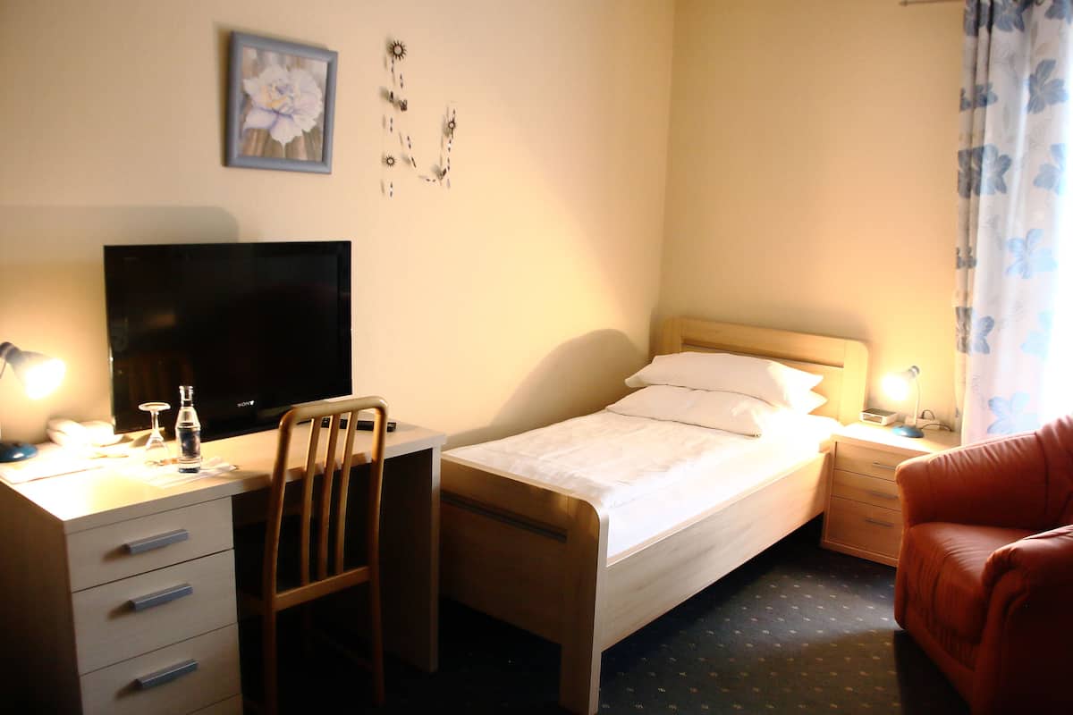 Hotellihuone, jossa on sänky, työpöytä, jossa on televisio, tuoli, yöpöytä ja punainen nojatuoli.
