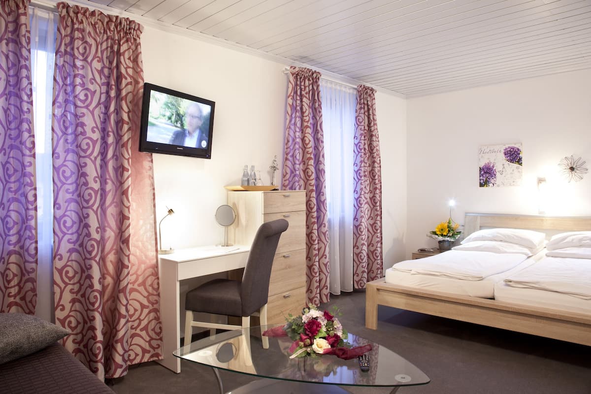Hotellihuone, jossa on sänky, työpöytä tuolilla, televisio ja verhot.