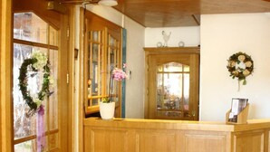 A wooden reception desk with a glass door, a potted plant, and a wreath on the wall. - Bimesmeier Gasthof & Pension (Koesslarn)