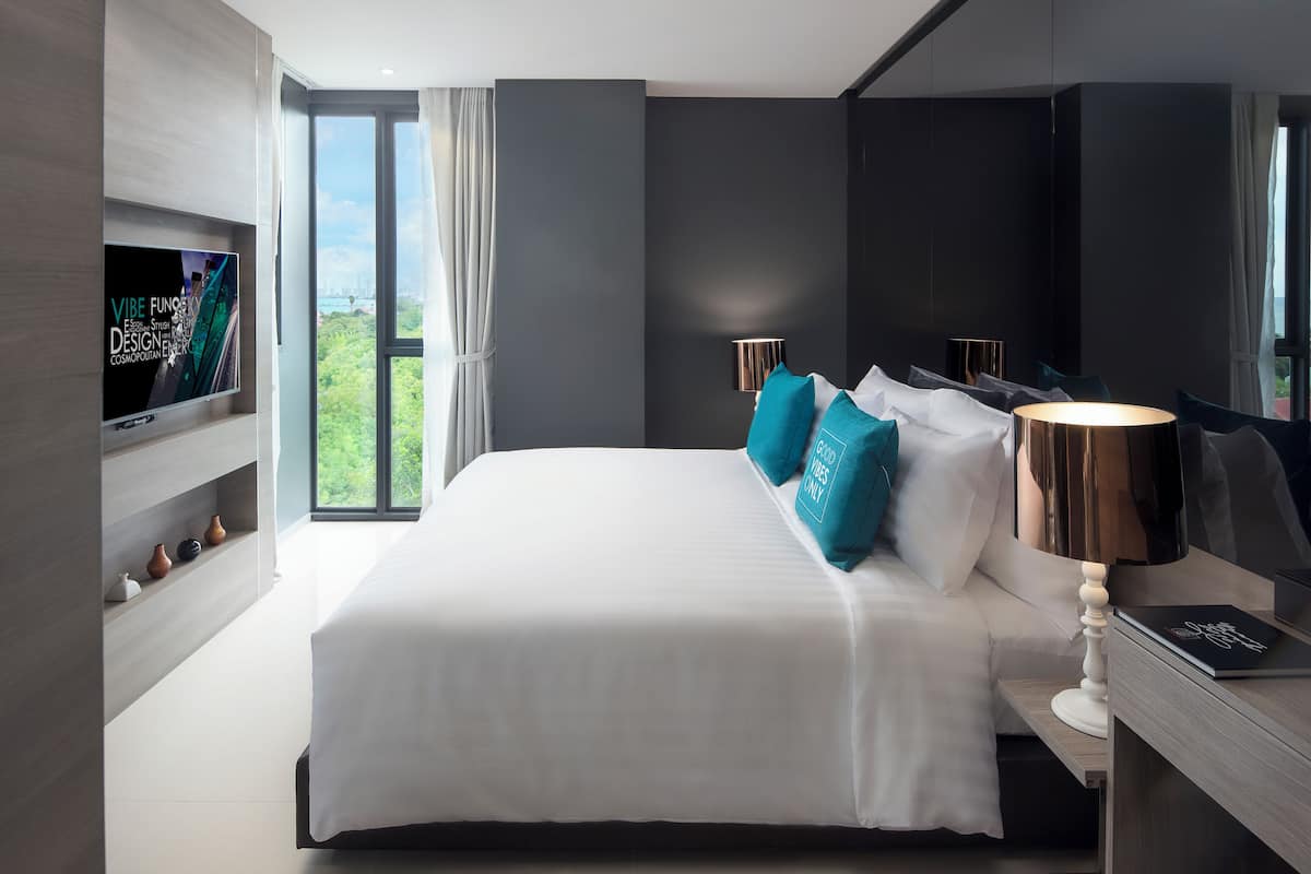 A modern hotel room with a large bed, a TV mounted on the wall, and a view of the outdoors.