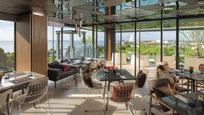 Un espace repas moderne avec des tables en verre et des chaises en métal, de grandes fenêtres offrant une vue sur la ville.