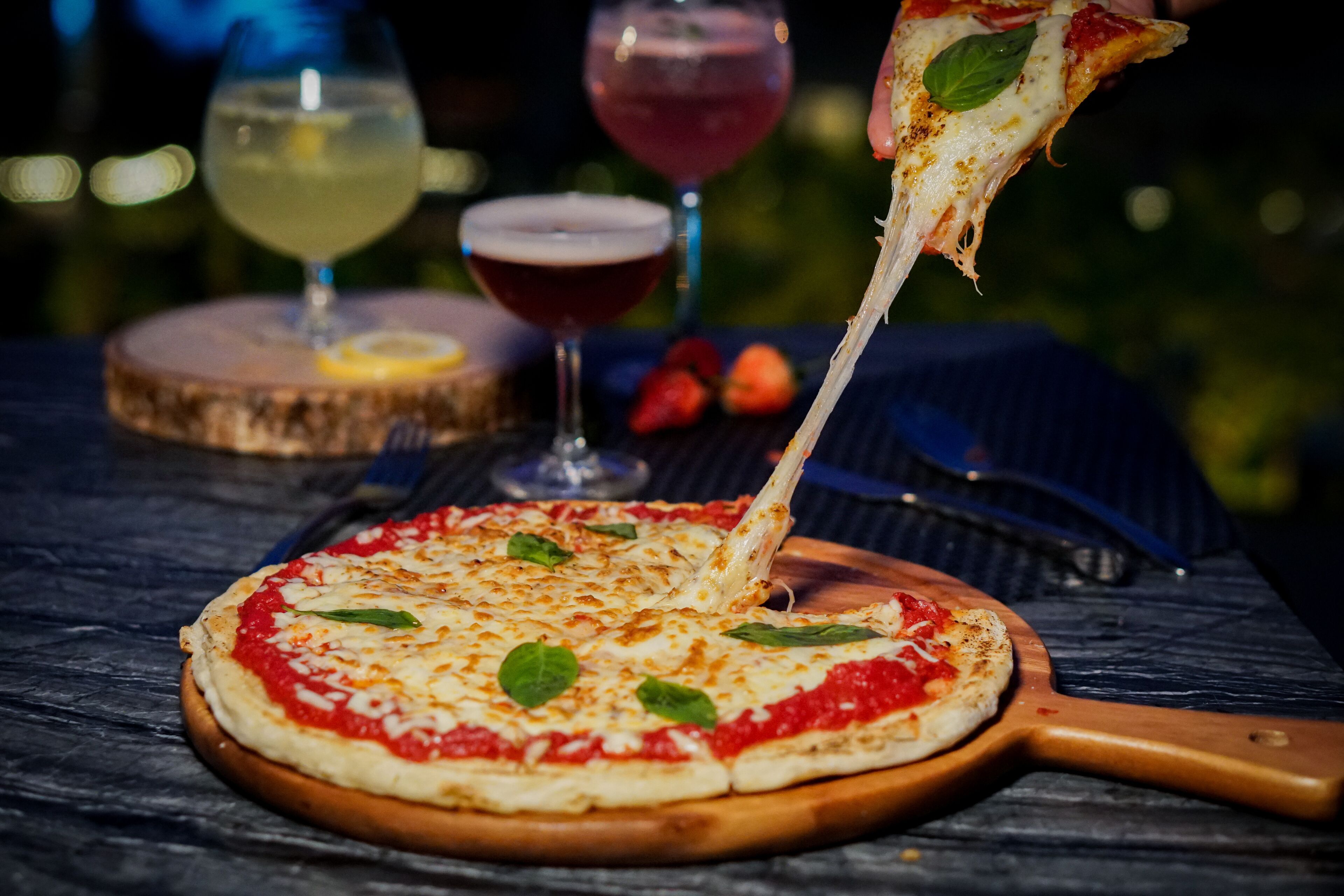 A pizza on a wooden board with a pizza cutter beside it.