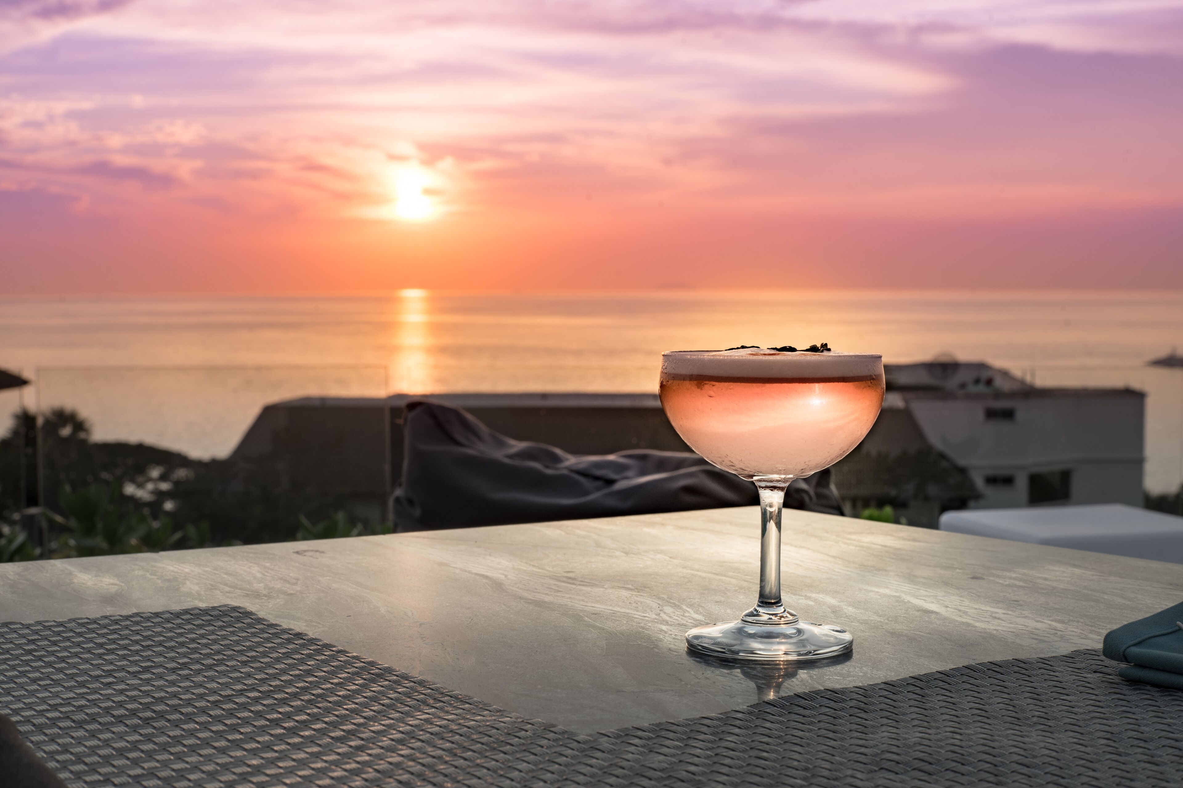 Una copa de cóctel sobre una mesa con vista al atardecer.