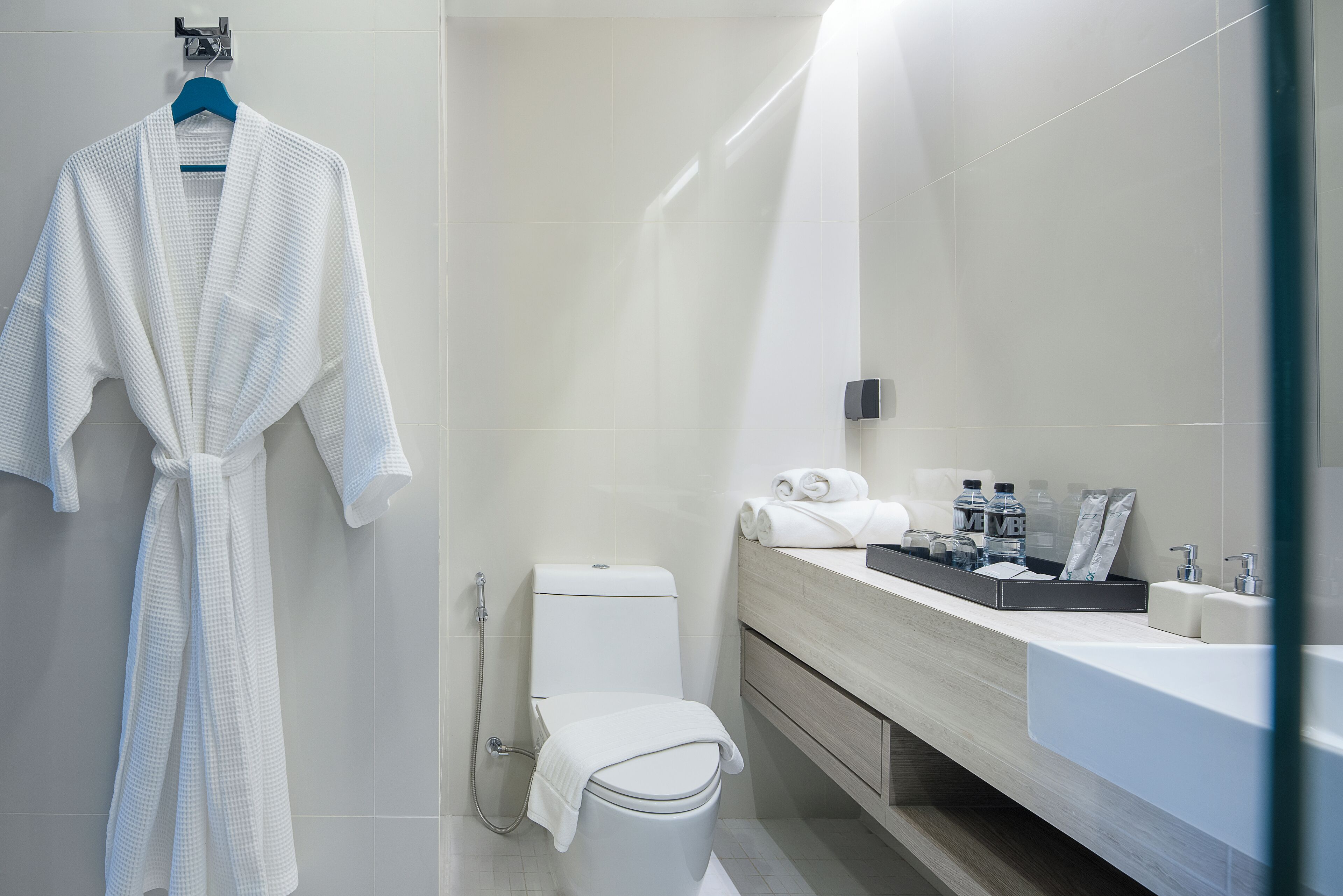 A modern bathroom with a toilet, sink, and a robe hanging on the wall.