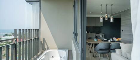 A modern balcony with a bathtub, a dining area with chairs, and a kitchen in the background.