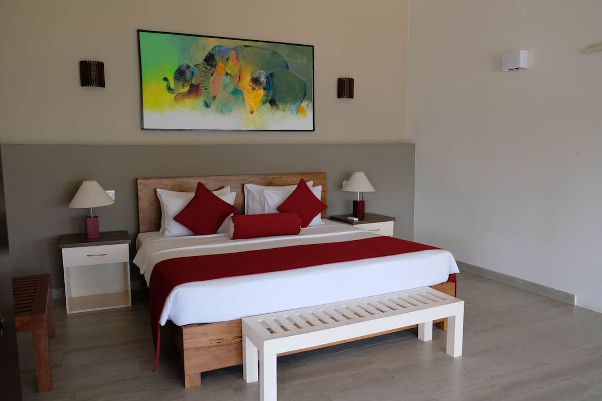 A modern bedroom with a wooden headboard, a large bed with red and white bedding, two bedside tables with lamps, and a bench at the foot of the bed.