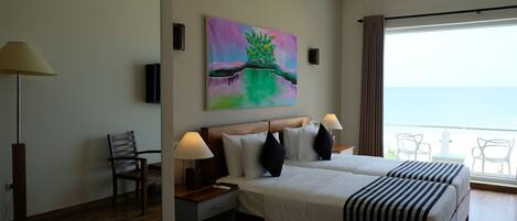 A hotel room with a large bed, two bedside tables with lamps, a chair, a painting on the wall, and a balcony with chairs.