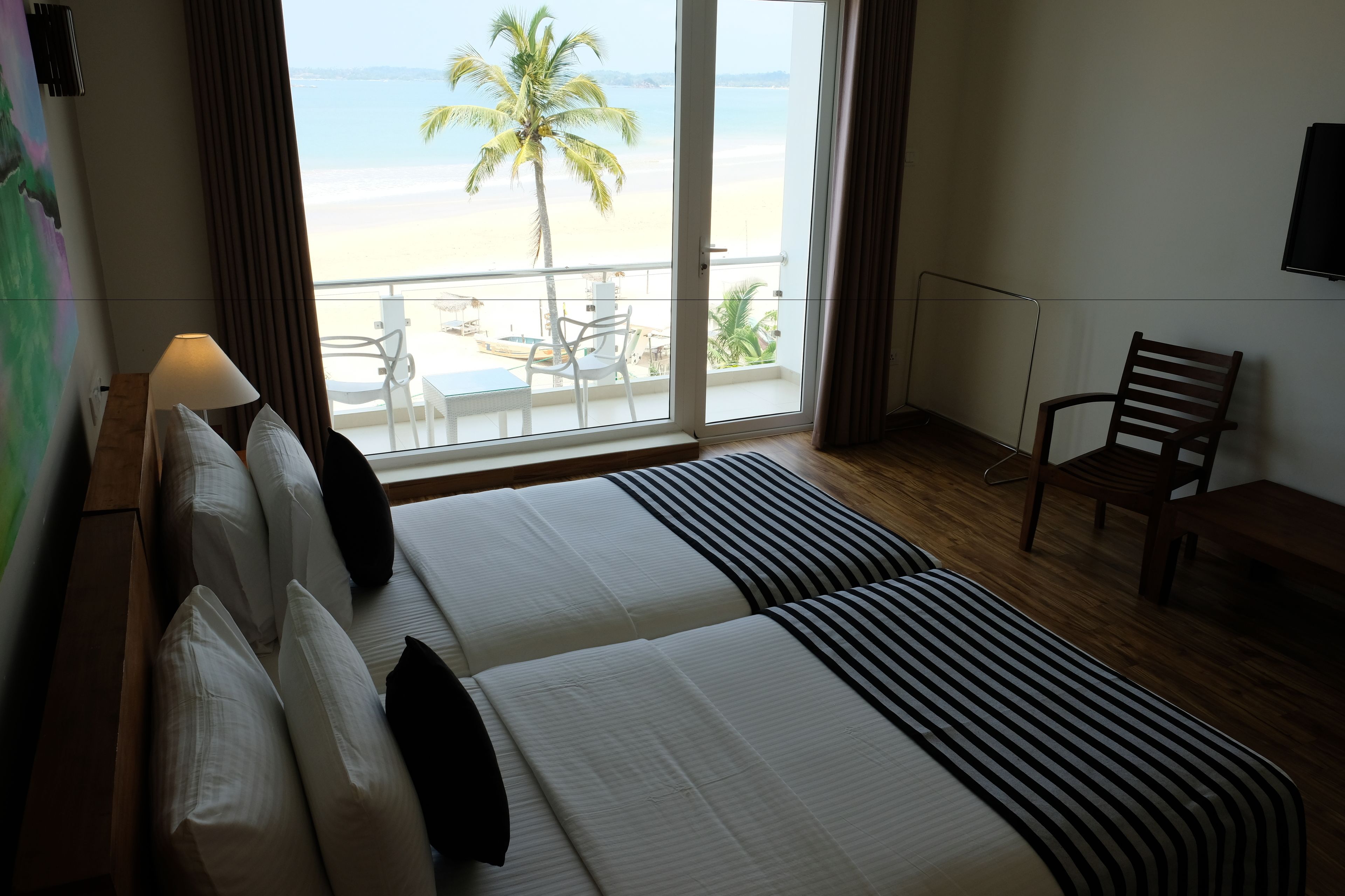 Habitación de hotel con dos camas, vista a la playa, una silla y una mesa.