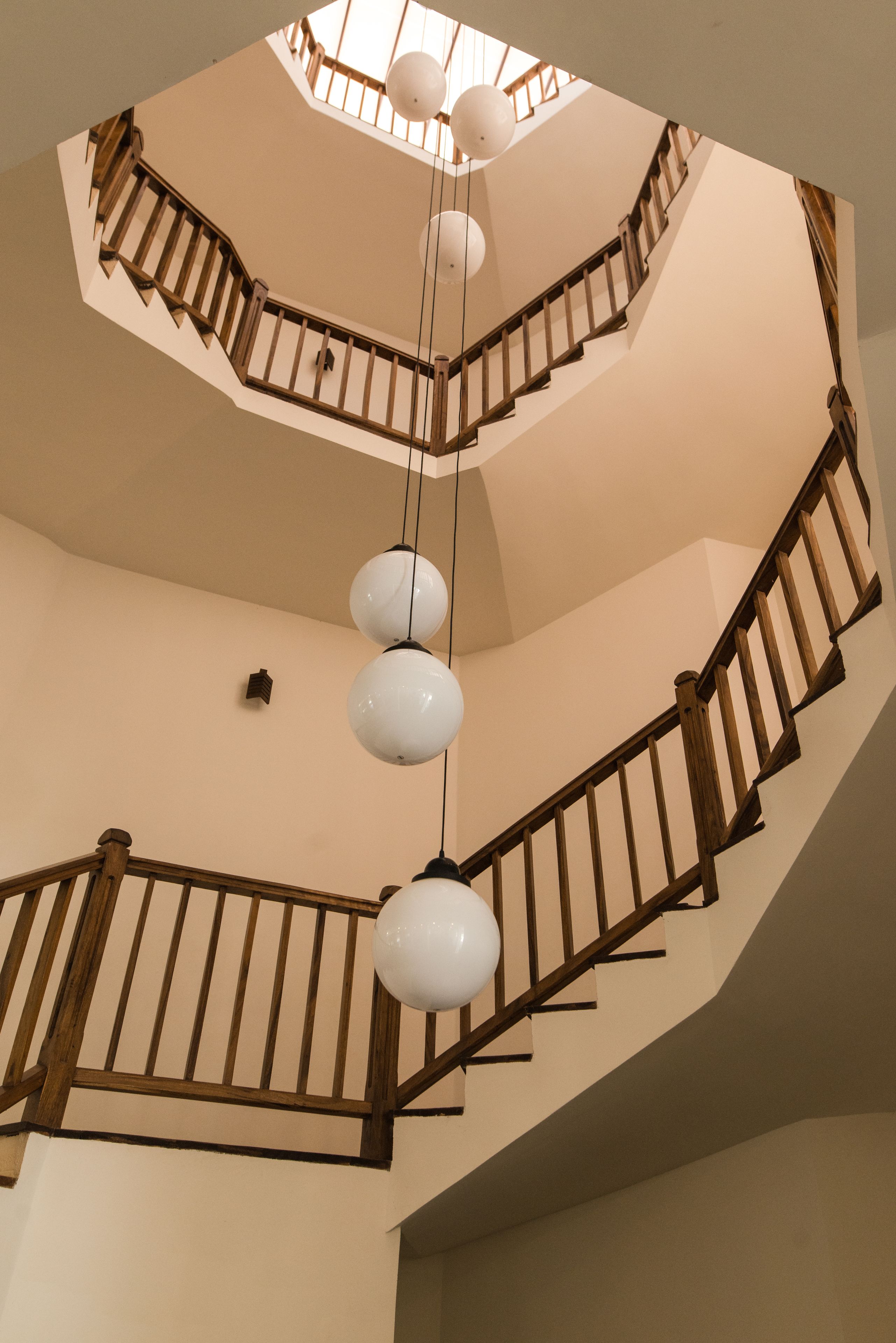A multi-level interior with a spiral staircase, wooden railings, and hanging spherical light fixtures.