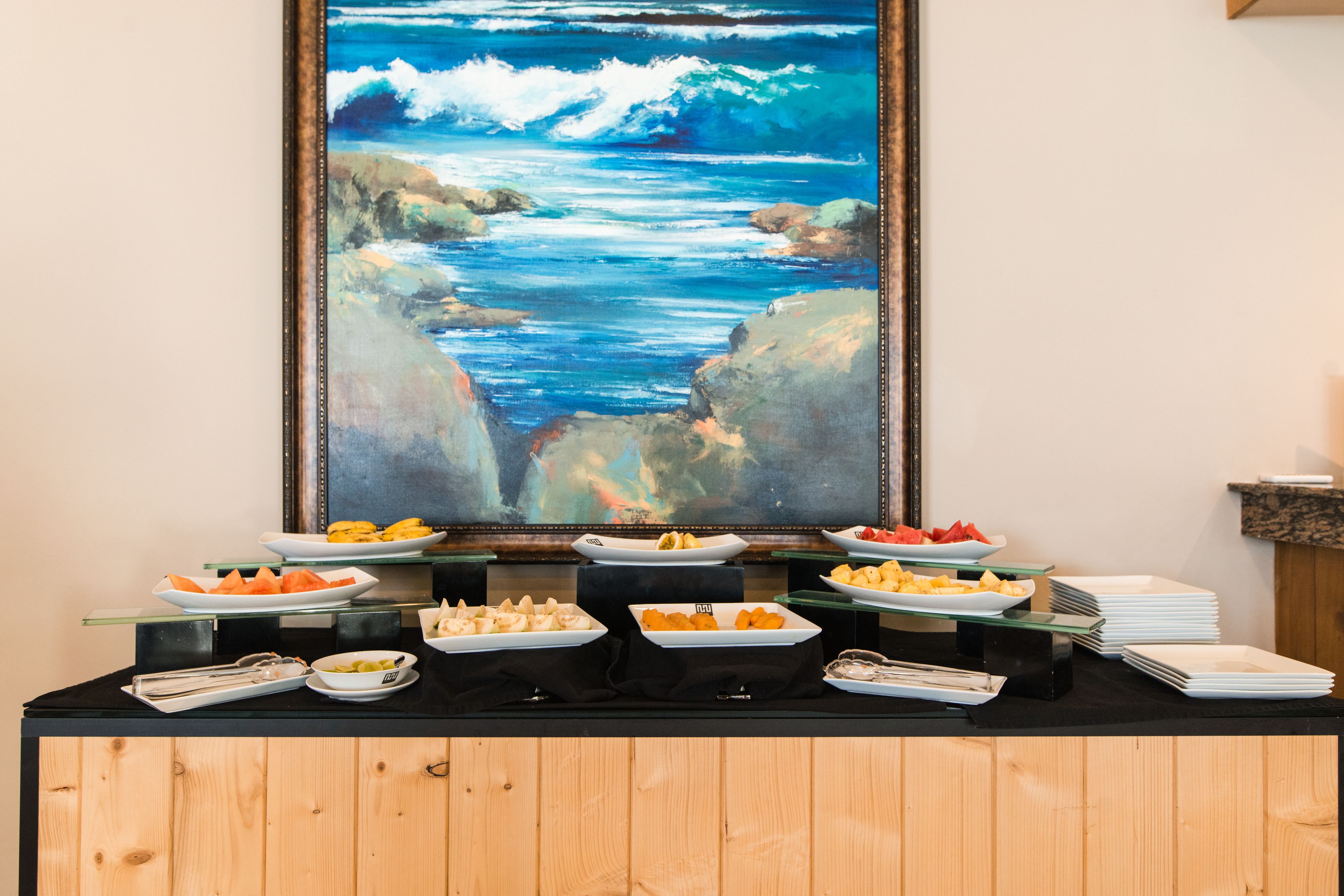 A buffet table with various food items and a large painting of a coastal scene.