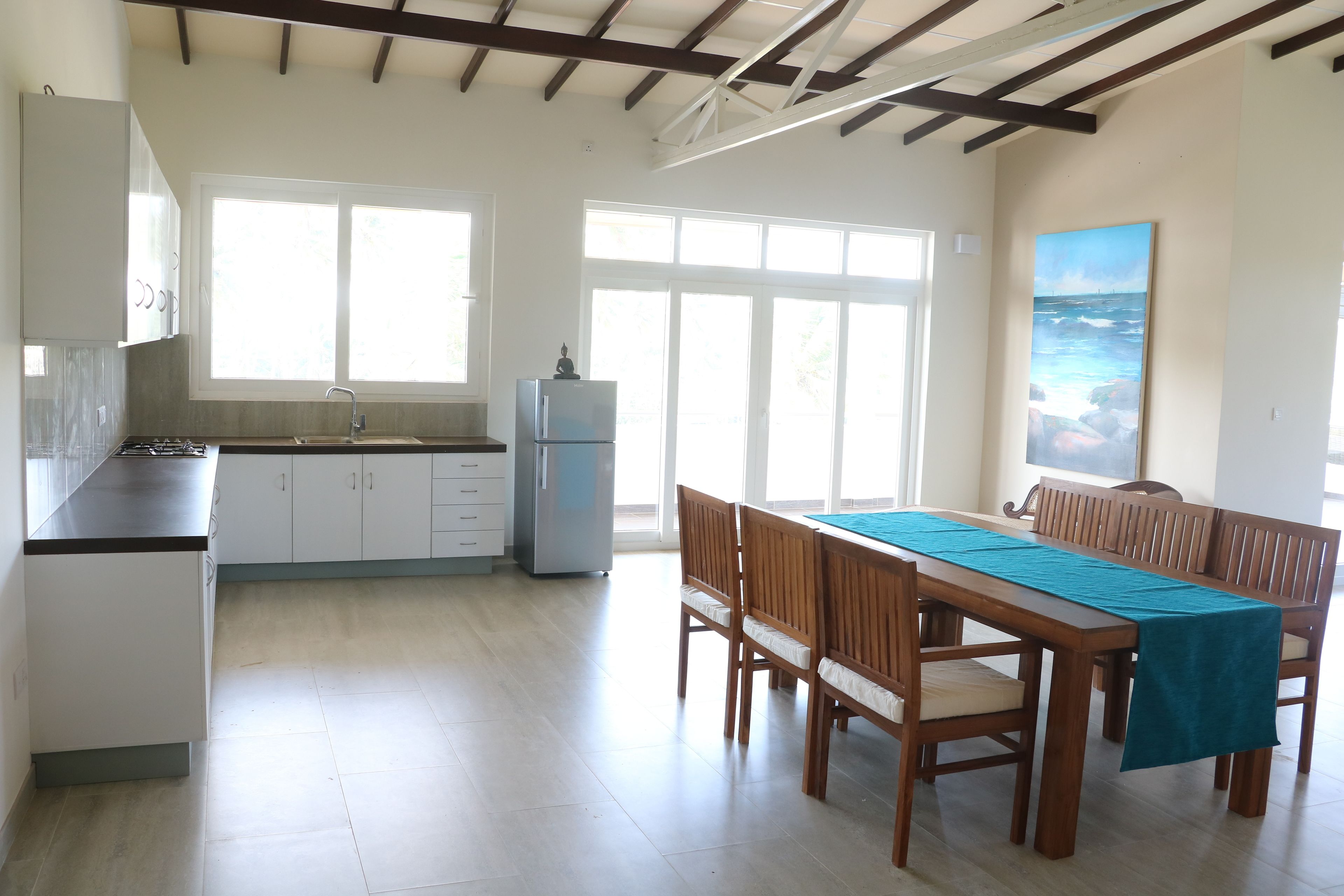 A spacious kitchen with a dining area, large windows, and a painting of a seascape.