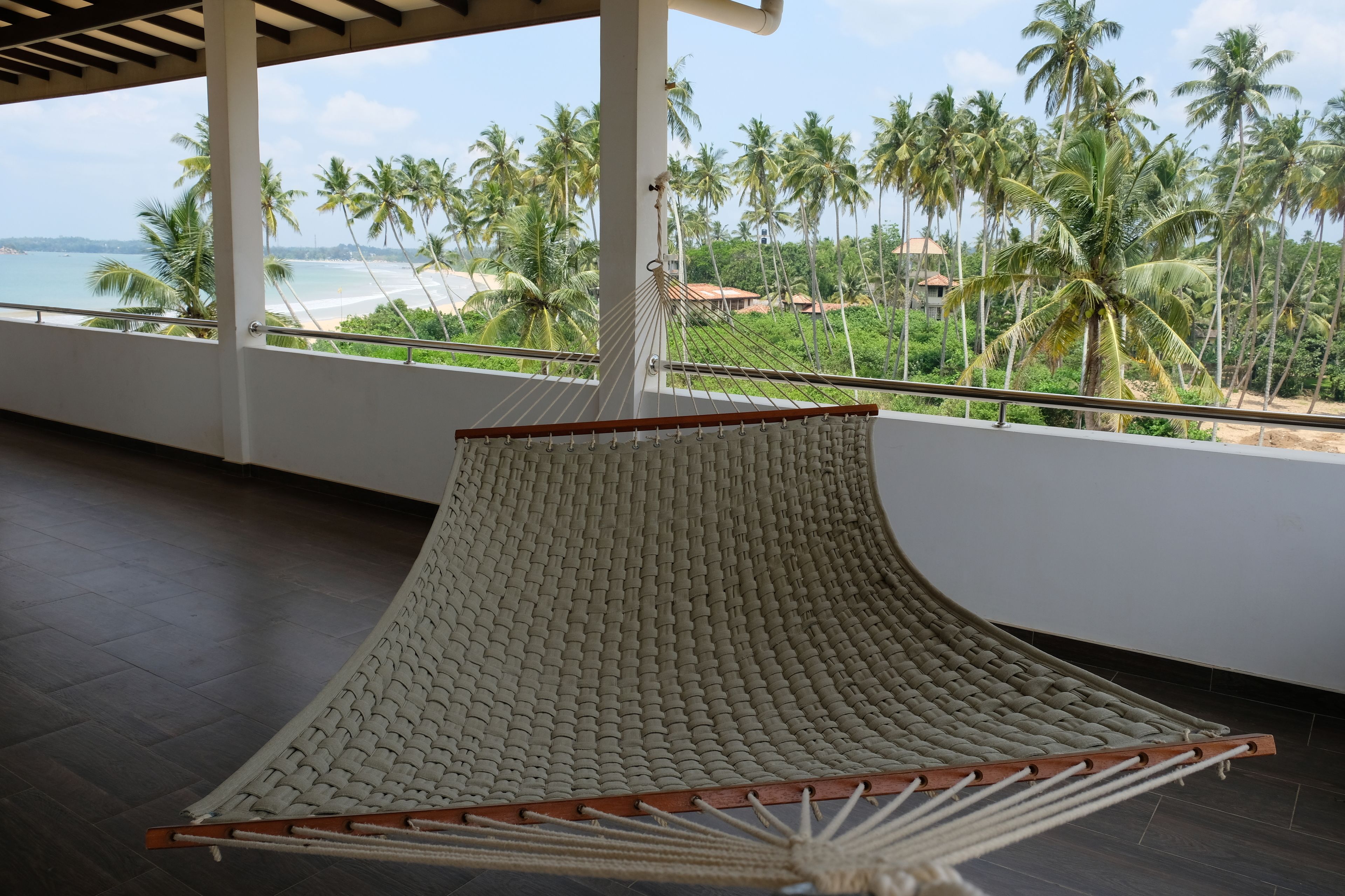 A hammock chair with a view of a beach and palm trees.
