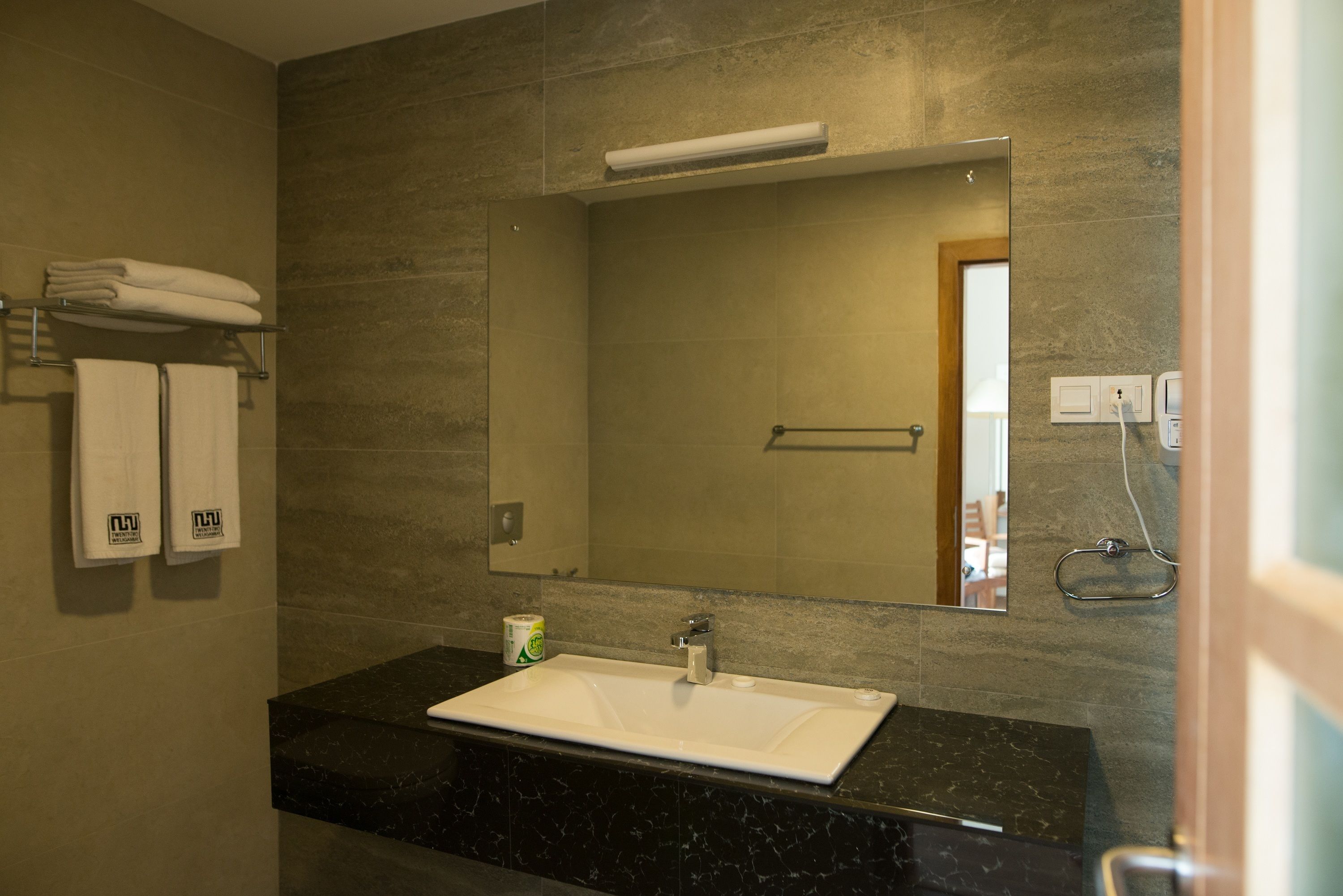 A bathroom with a white sink, dark marble countertop, and a large mirror.