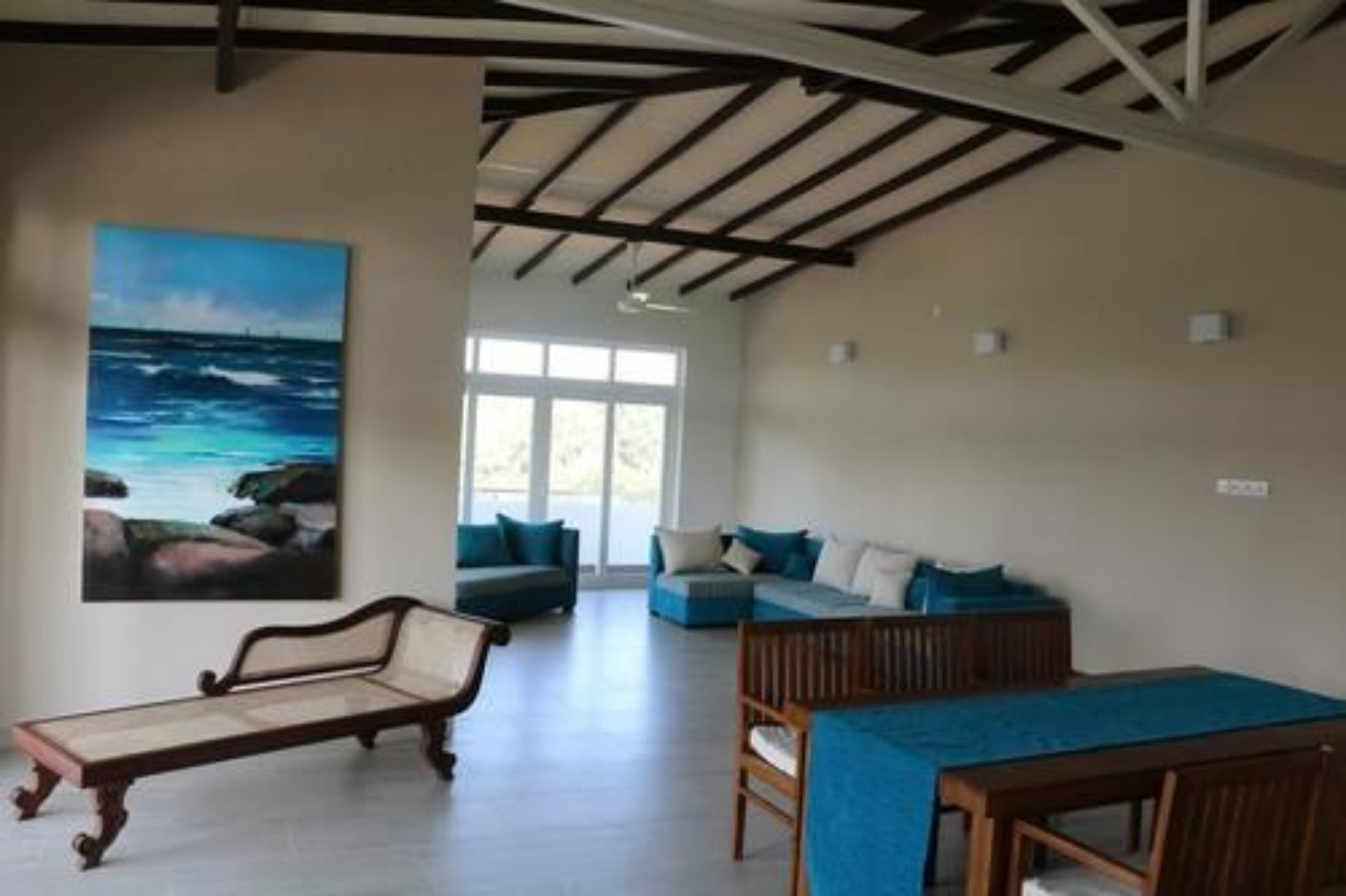 A spacious room with a large window, a painting of the ocean, and a blue sofa.