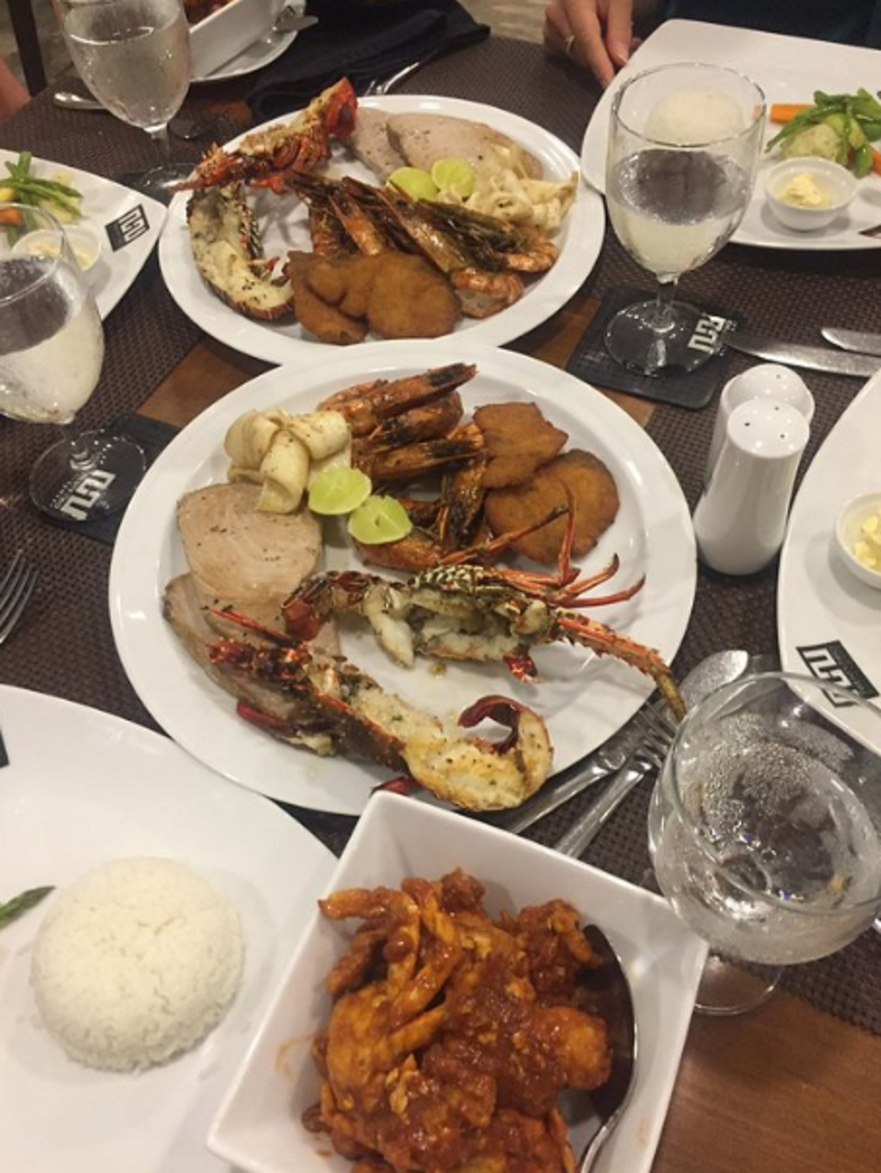 A dining table with plates of seafood, including lobsters and shrimp, and a bowl of rice.