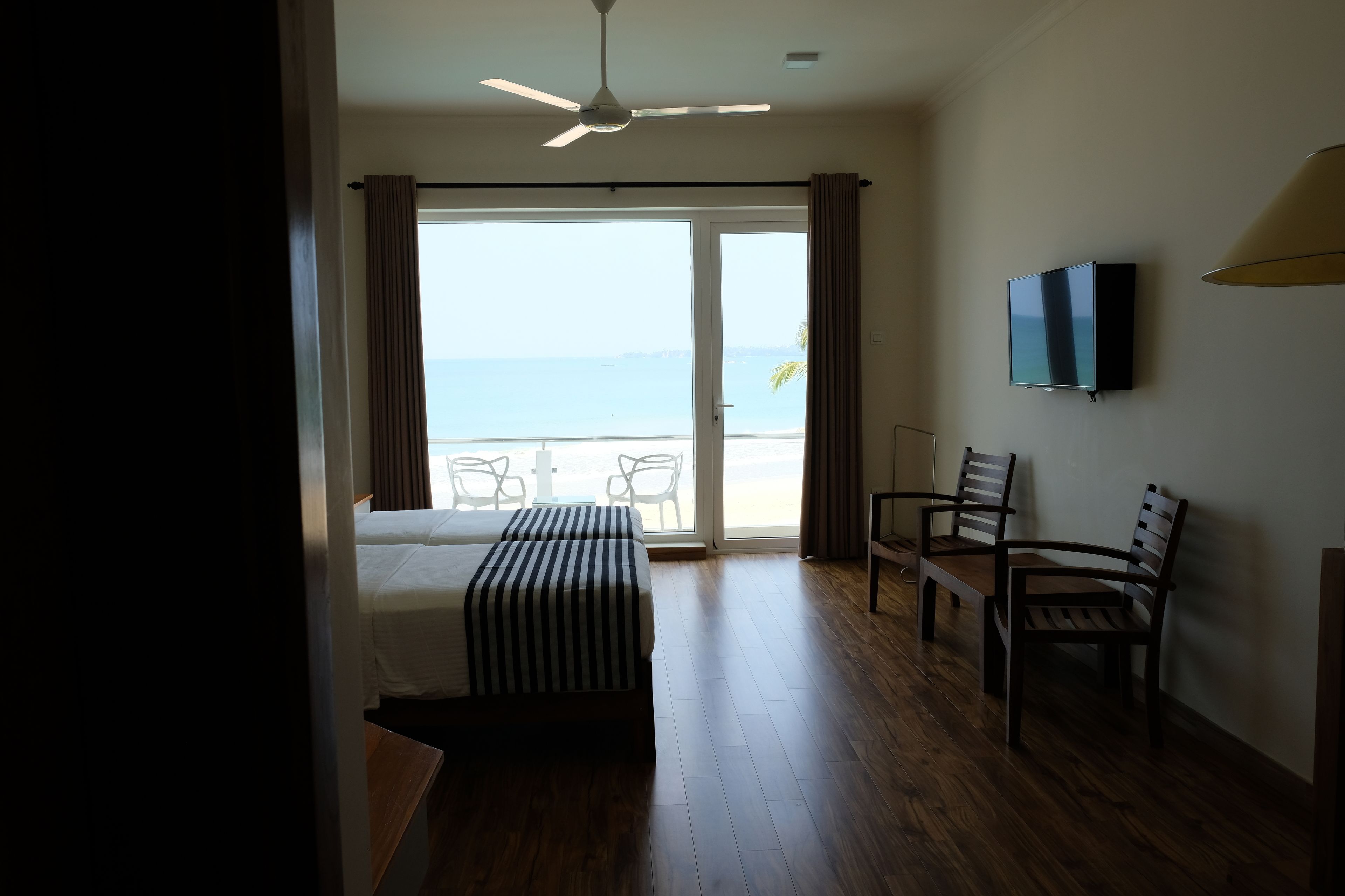 Habitación de hotel con cama, escritorio, silla, televisor y balcón con vista al mar.