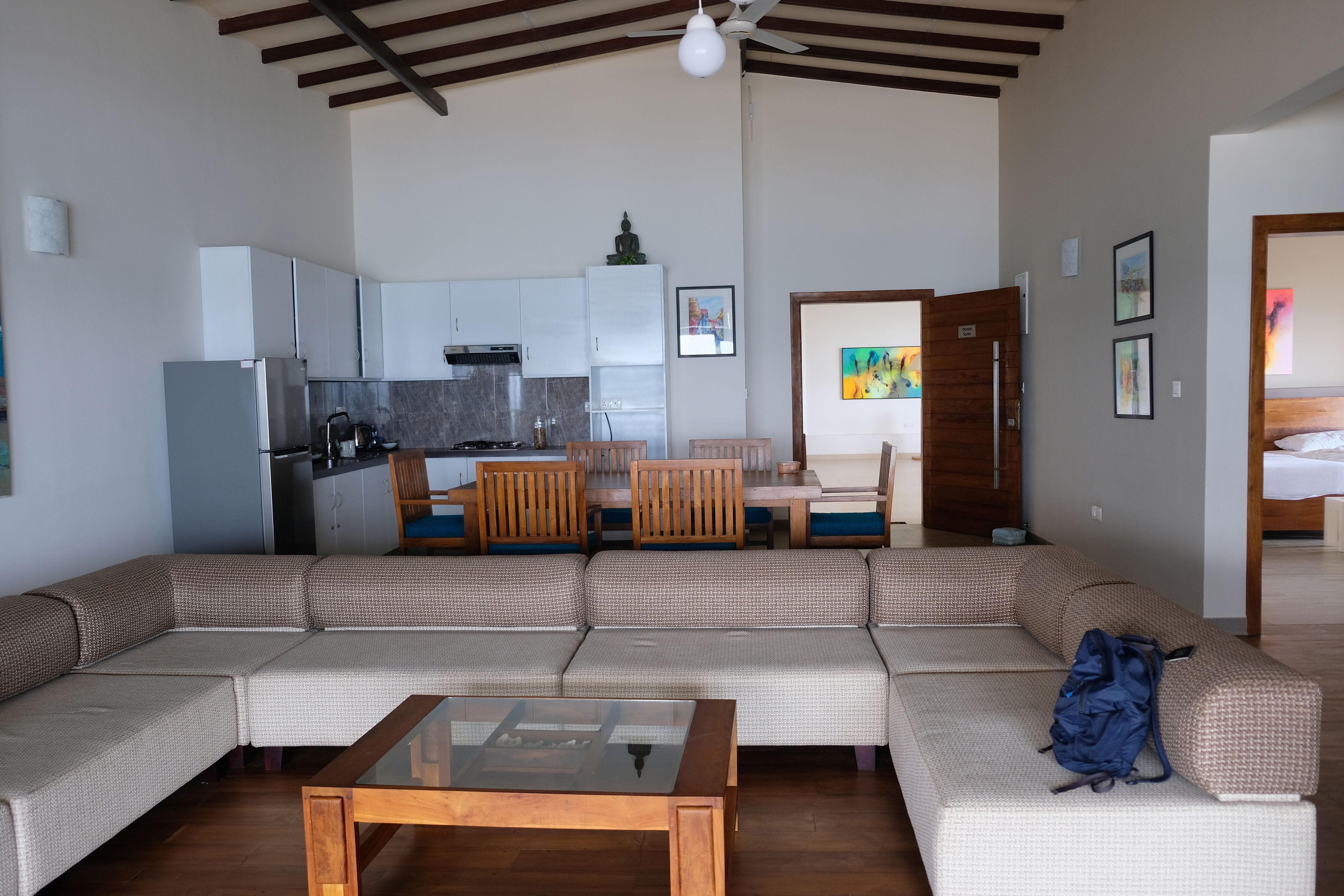 Uma sala de estar moderna com sofá em formato de L, mesa de centro de vidro e área de jantar com cadeiras e mesa de madeira.