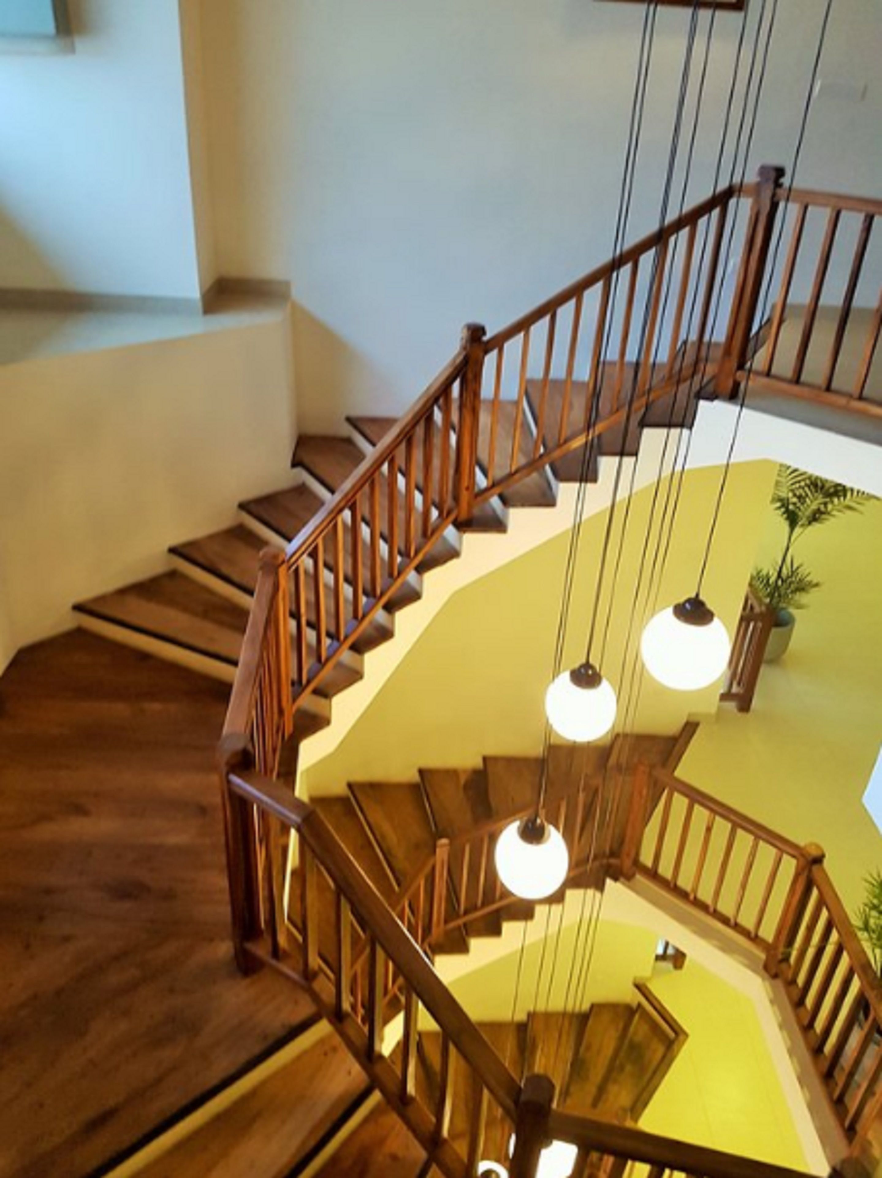 Una escalera de madera con barandilla, varios peldaños e iluminación colgante.