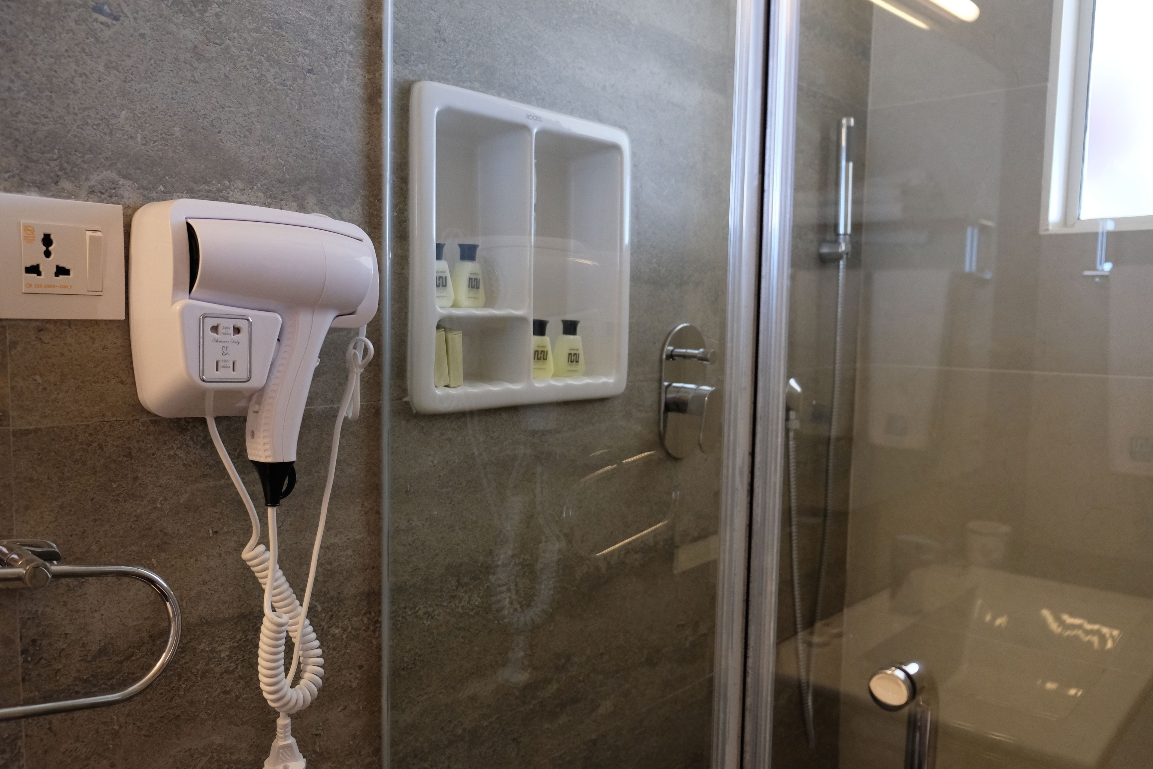 Un baño con secador de pelo, cabina de ducha de vidrio y dispensador de jabón.