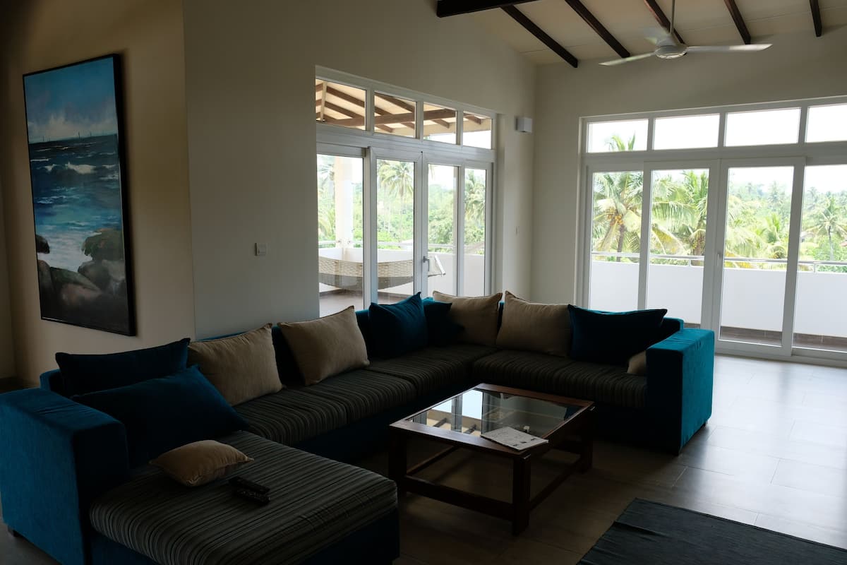 A living room with a sectional sofa, a glass coffee table, and large windows offering a view of the outdoors.